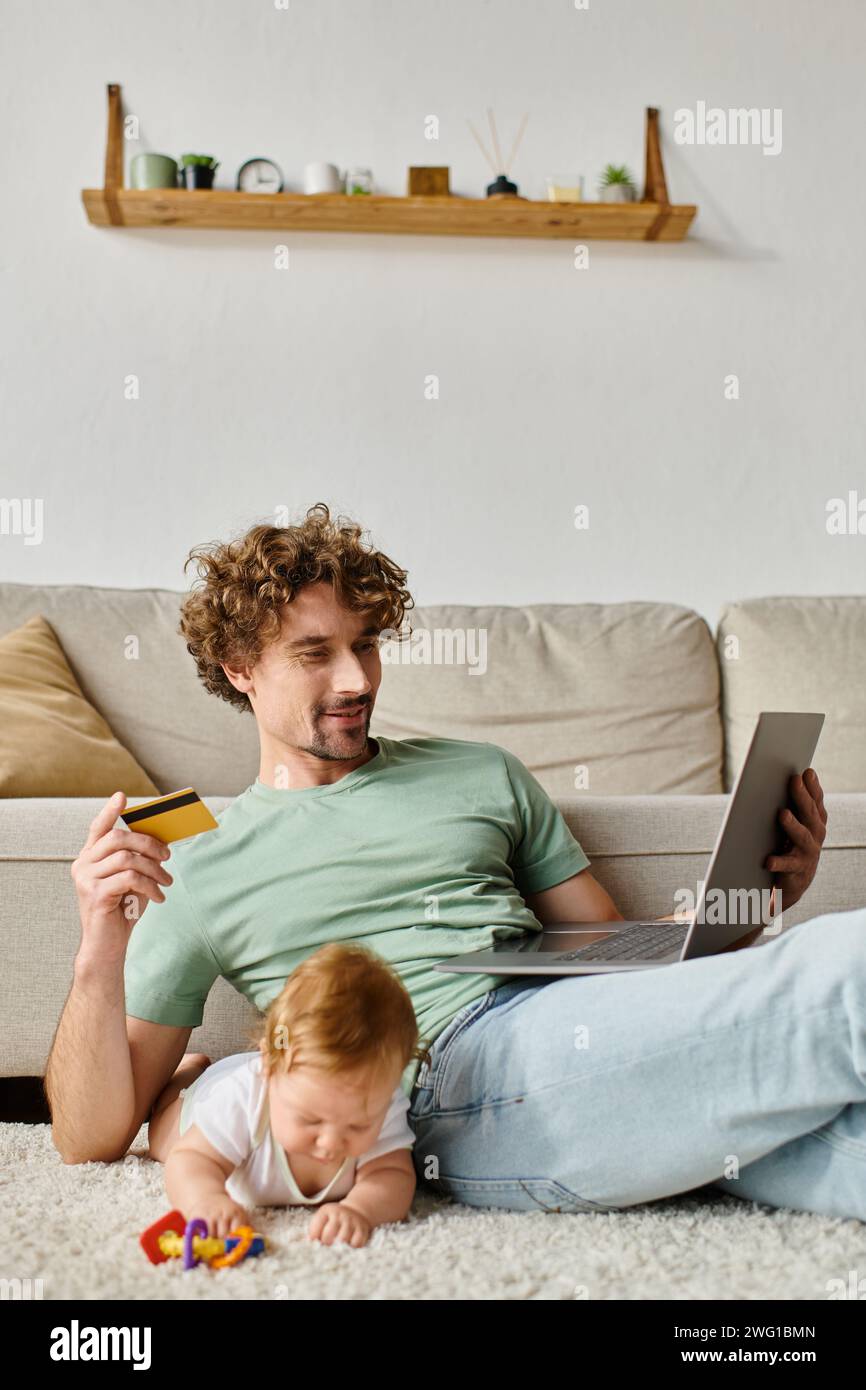 Glücklicher Vater mit Kreditkarte beim Online-Shopping in der Nähe von Baby Boy, der mit Rassel spielt Stockfoto