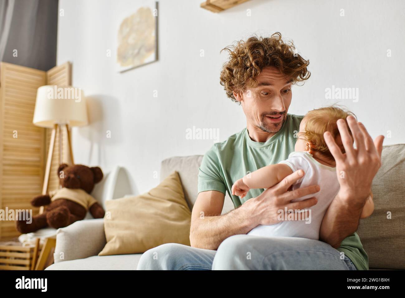 Fröhlicher Vater mit Bart und Blick auf seinen kleinen Sohn in einem gemütlichen Wohnzimmer, Vaterschaft und Freude Stockfoto