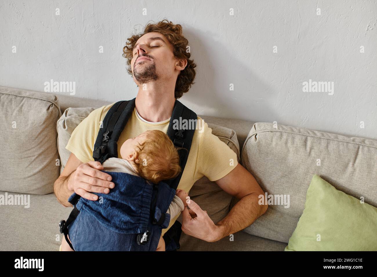 Lockiger Vater, der mit dem Kleinkind in der Babytrage im Wohnzimmer schläft, Vaterschaft und Liebe Stockfoto