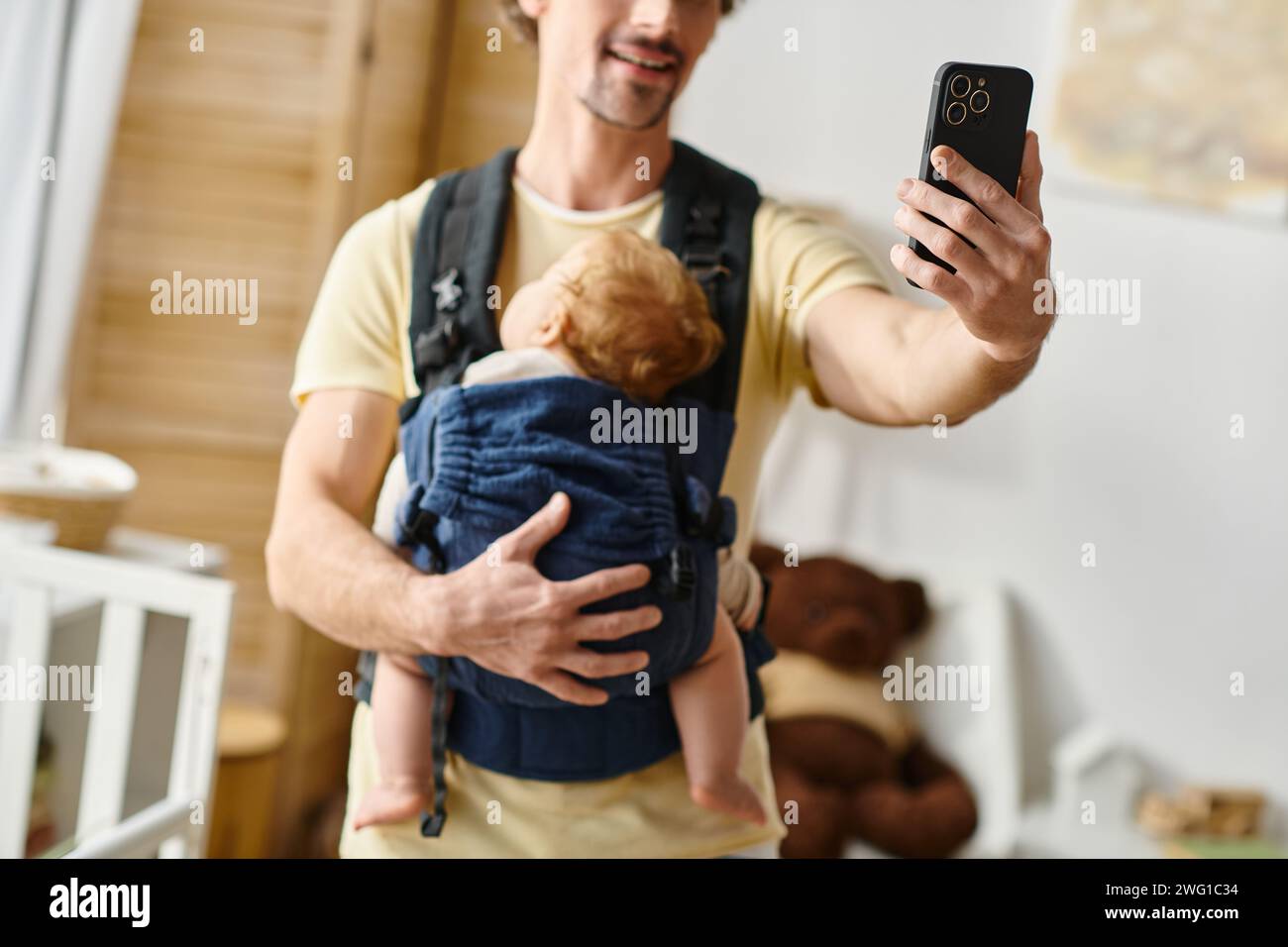 Ein abgeschnittener Vater macht Selfie mit schlafendem Baby in Tragetasche, Vaterschaft und modernem Elternkonzept Stockfoto
