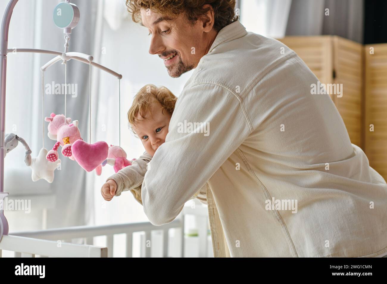 Liebevoller alleinerziehender Vater, der seinen kleinen Sohn in der Nähe des Babymobils hält, im Kinderzimmer, Vaterschaft und Liebe Stockfoto