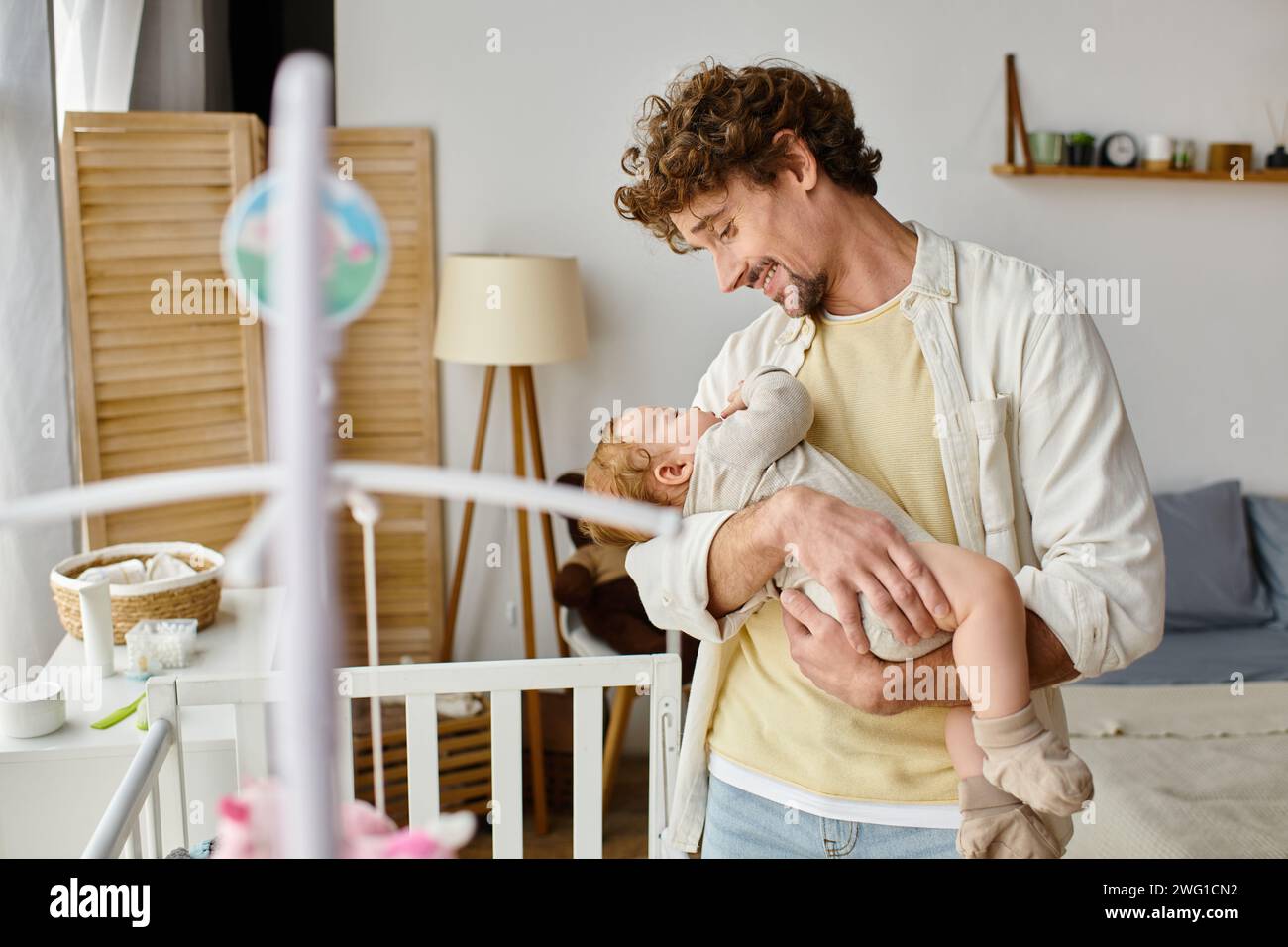 Glücklicher alleinerziehender Vater, der seinen kleinen Sohn in Armen in der Nähe einer Babykrippe hält, in Kinderzimmer, Vaterschaft und Liebe Stockfoto