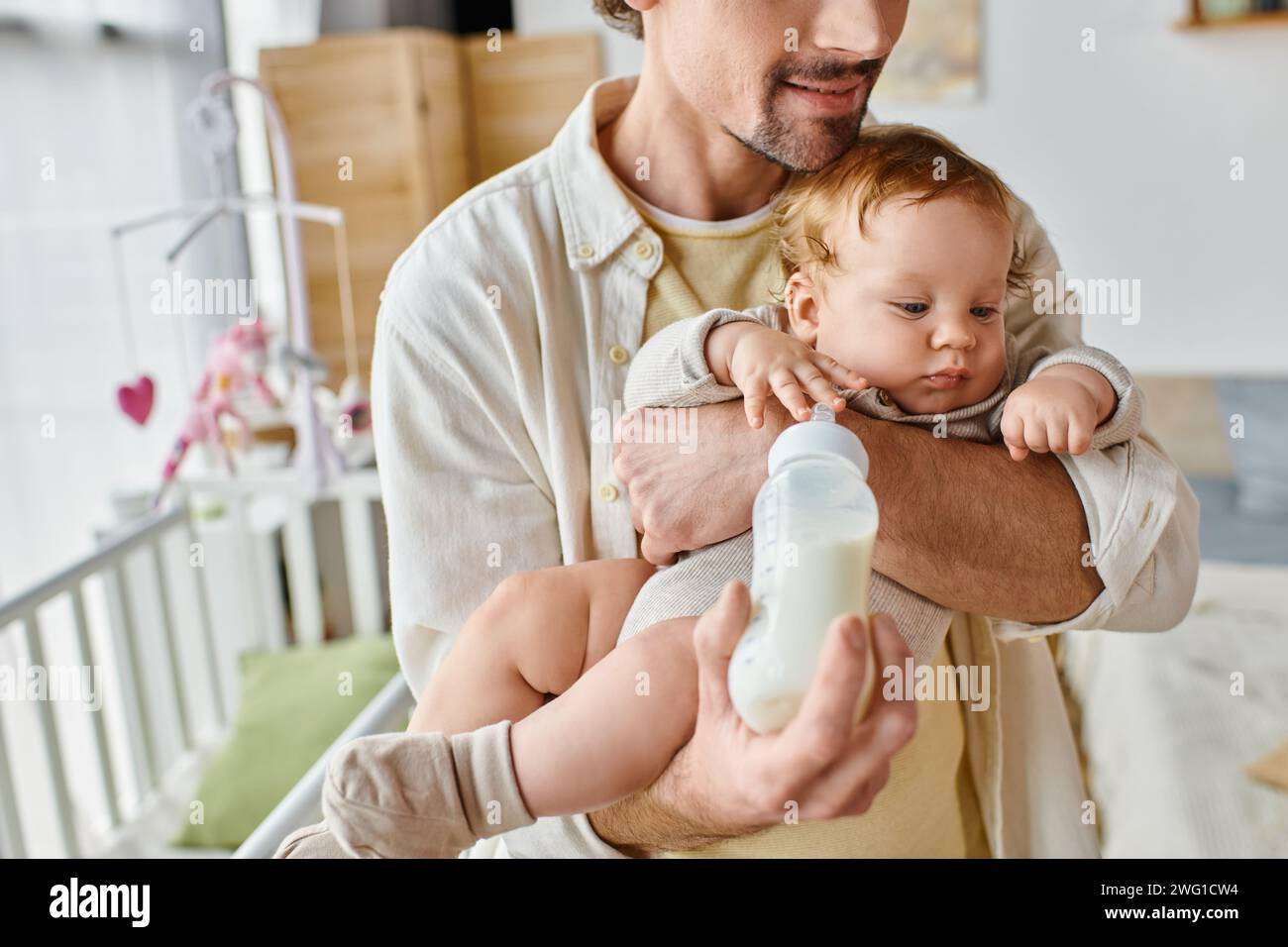 Ein abgeschnittener Vater füttert seinen kleinen Sohn aufmerksam mit Milch in der Babyflasche, Vaterschaft und Pflege Stockfoto