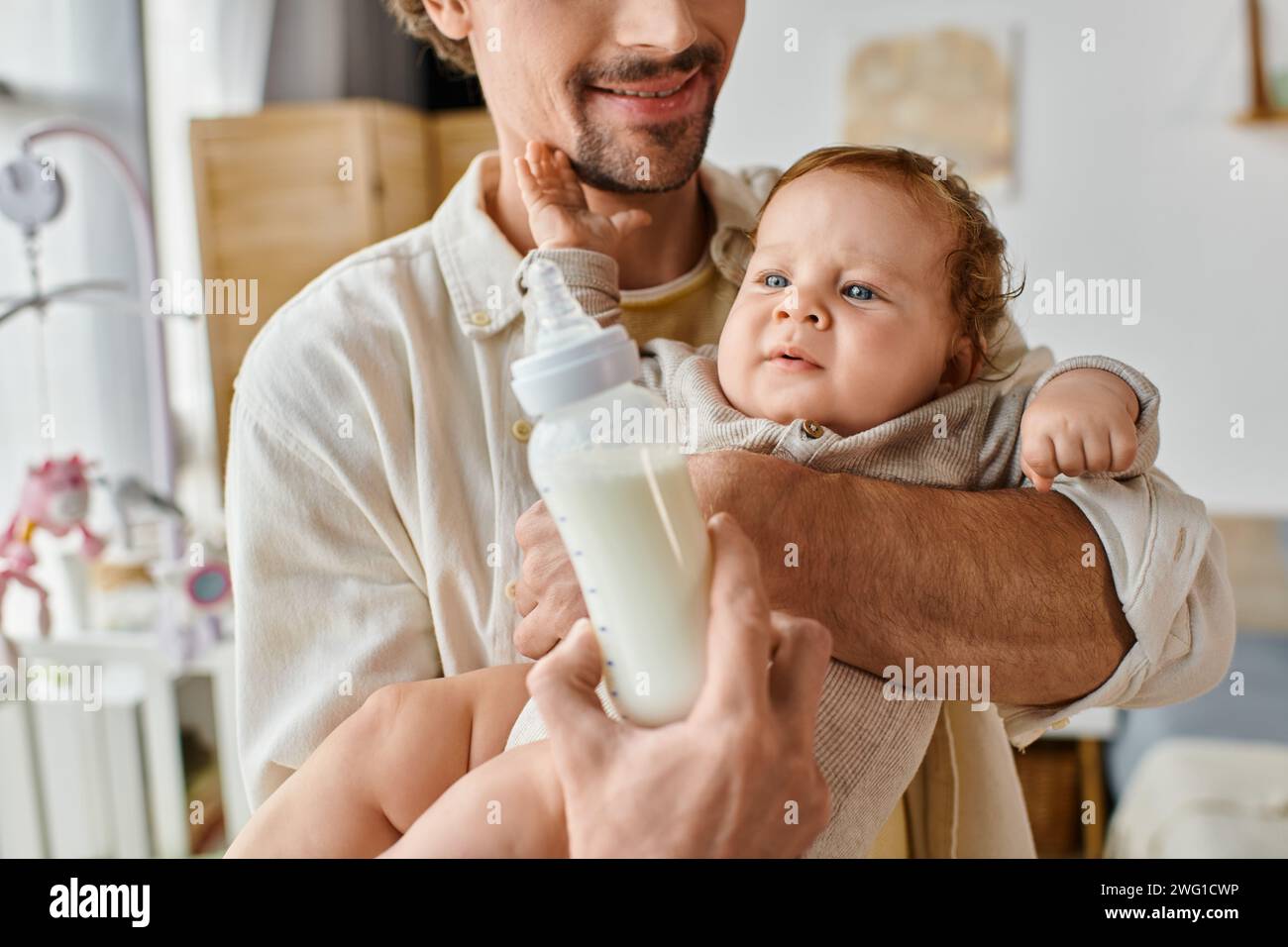 Glücklicher Vater füttert seinen kleinen Sohn aufmerksam mit Milch in der Babyflasche, Vaterschaft und Pflege Stockfoto