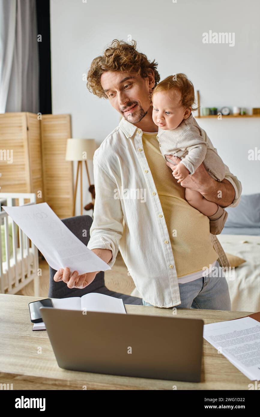 Glücklicher und bärtiger Vater, der ein Kind im Arm hält und Dokumente ansieht, Work Life Balance Stockfoto
