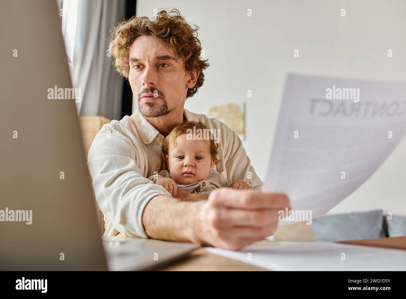 Beschäftigter alleinstehender Vater, der den Säuglingssohn hält und sich bei der Arbeit von zu Hause aus in die Hände zieht, Work-Life-Balance Stockfoto