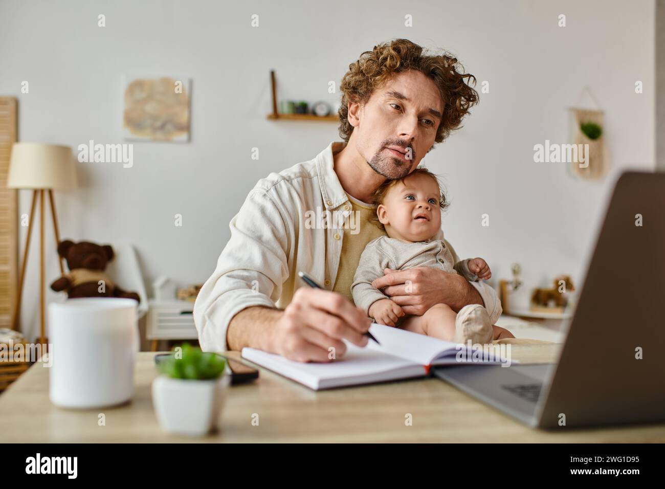 Beschäftigter alleinstehender Vater hält seinen kleinen Sohn in Händen, während er von zu Hause aus arbeitet, Work-Life-Balance Stockfoto