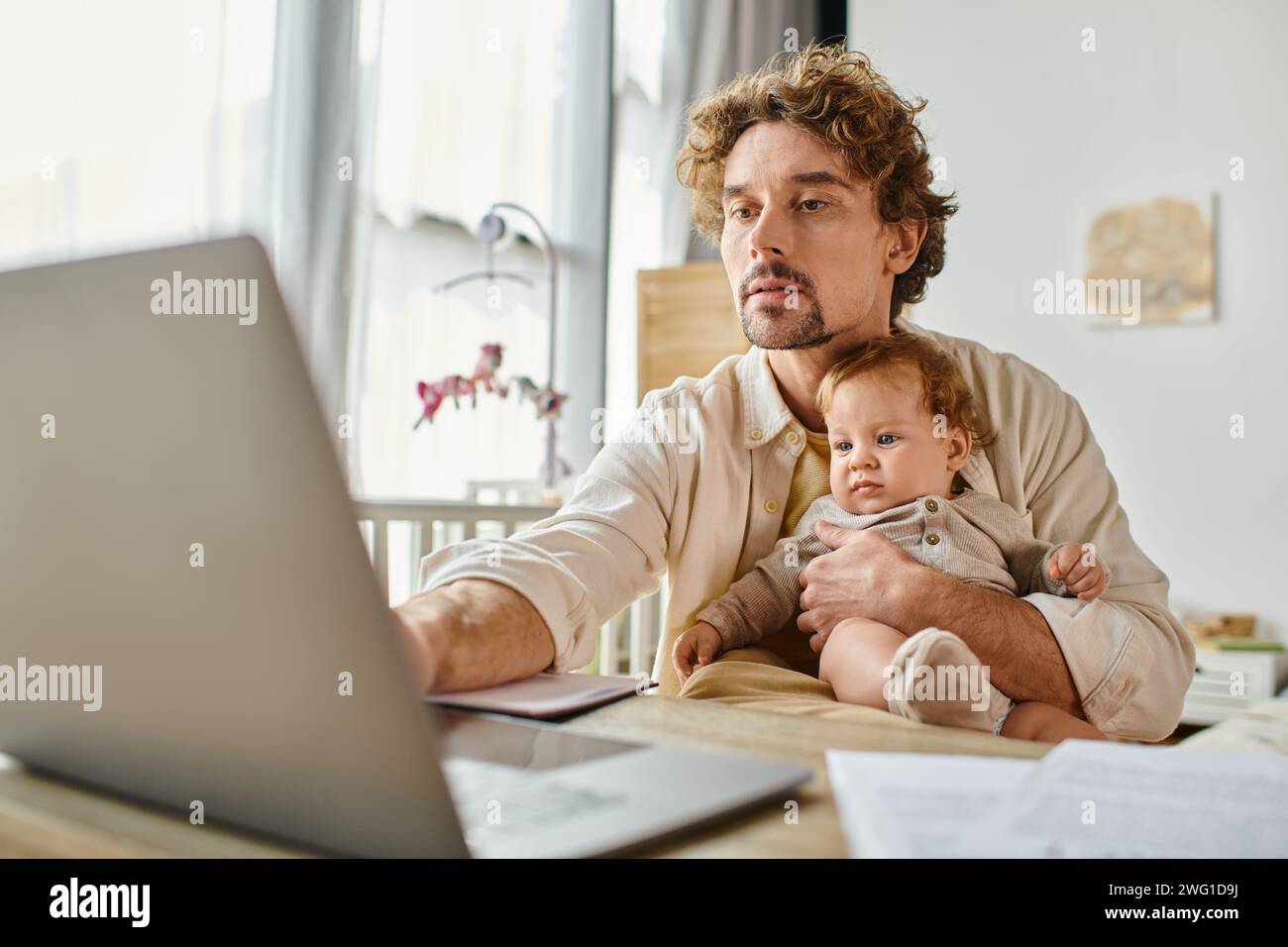 Beschäftigter alleinstehender Vater hält seinen niedlichen Sohn in Händen, während er von zu Hause aus arbeitet, Work-Life-Balance Stockfoto