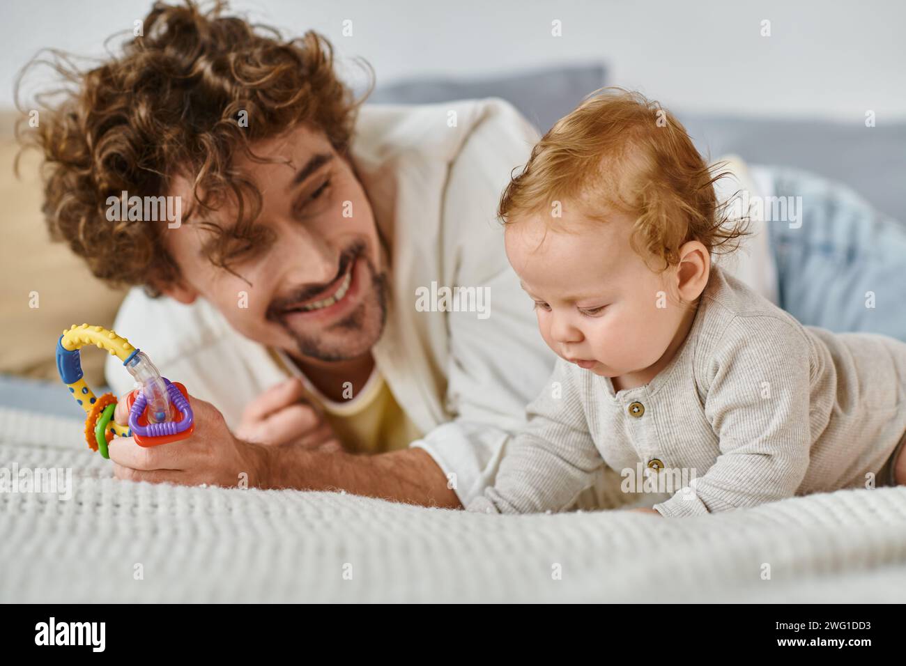 Alleinerziehender Vater, der eine bunte Rassel in der Nähe des kleinen Jungen im Schlafzimmer hält, Band zwischen Vater und Sohn Stockfoto