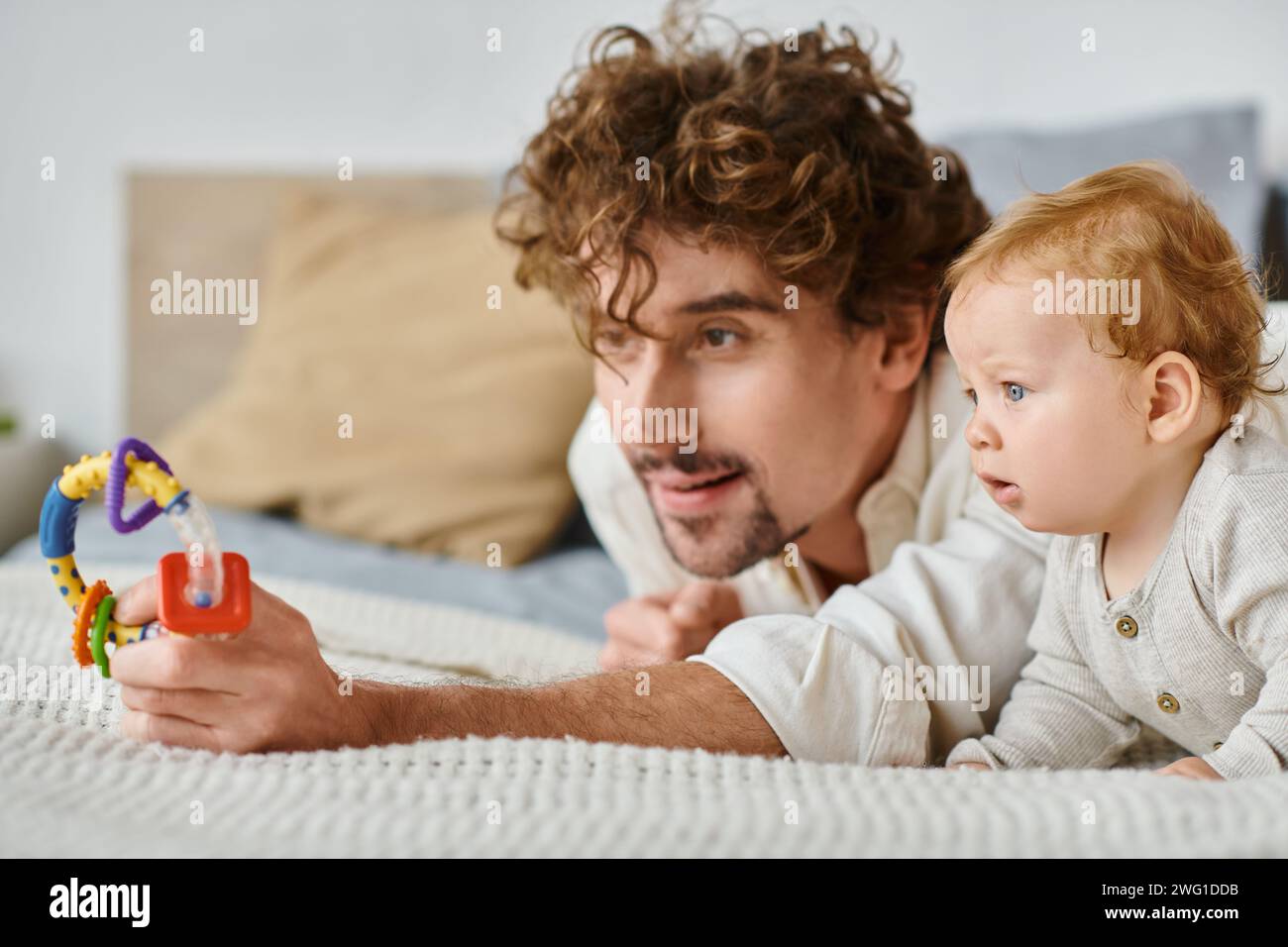 Alleinerziehender Vater und kleiner Junge, fasziniert von farbenfroher Rassel im Schlafzimmer, Bindung zwischen Eltern und Kind Stockfoto