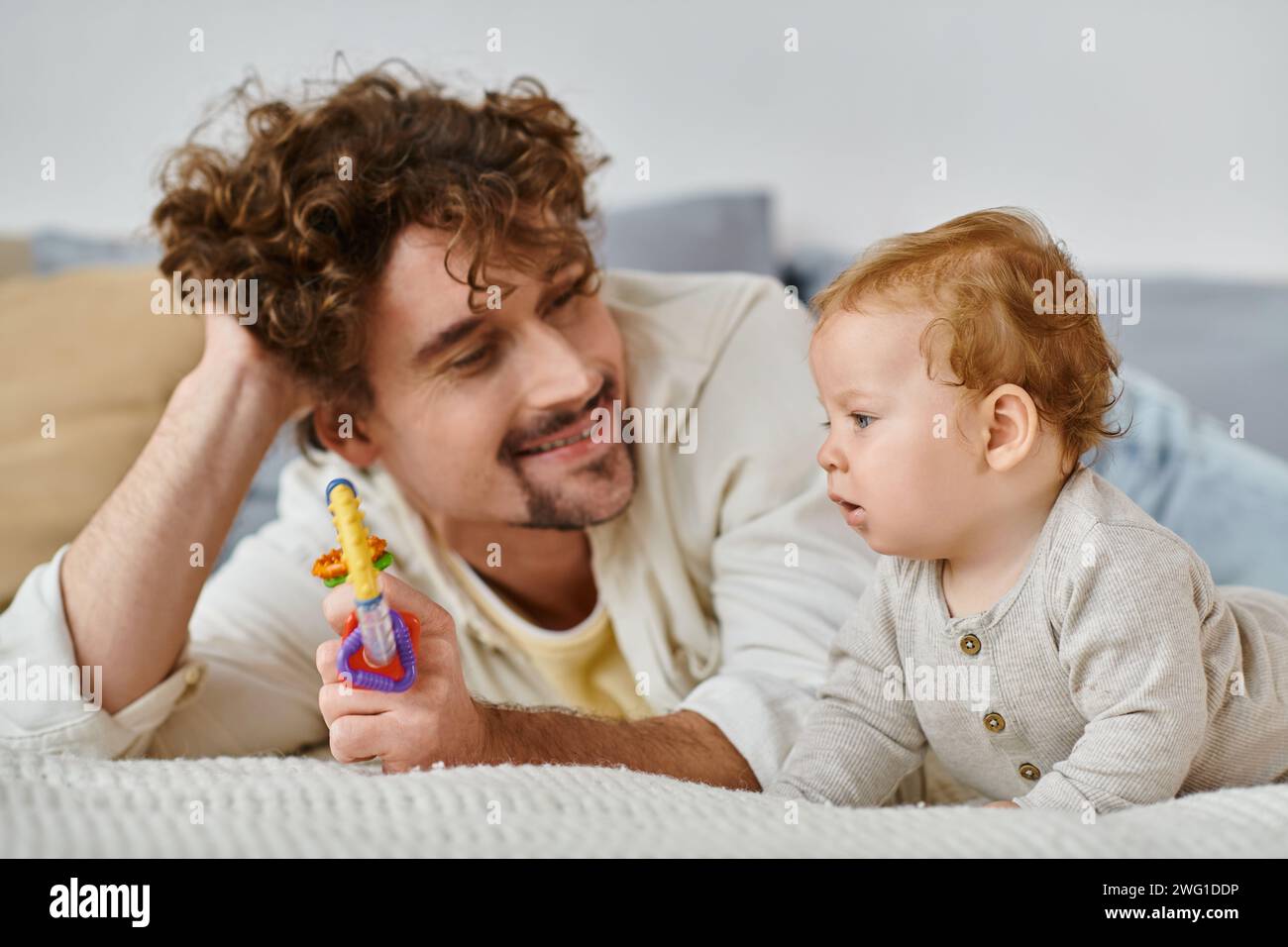 Glücklicher Mann, der dem kleinen Jungen im Schlafzimmer eine bunte Rassel zeigt, Band zwischen Vater und Sohn Stockfoto