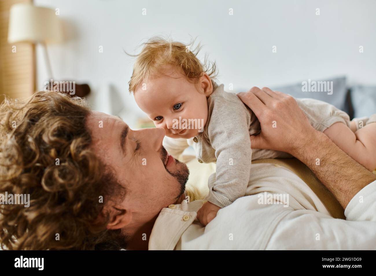 Glücklicher Mann mit lockigen Haaren und Bart, der sich mit seinem kleinen Sohn im Schlafzimmer umschließt, Liebe und Pflege Stockfoto