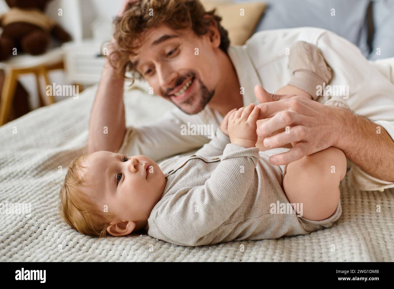 Niedlicher Junge, der auf dem Bett liegt und die Hand seines bärtigen, glücklichen Vaters hält, kostbare Momente Stockfoto