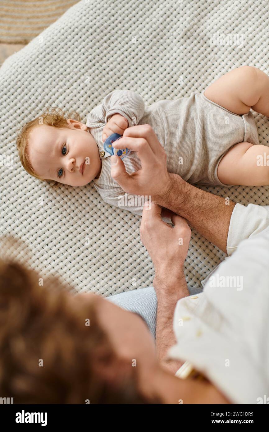 Blick von oben auf den kleinen Jungen, der seinen Vater mit Schnuller in der Hand, Vaterschaft und Liebe betrachtet Stockfoto