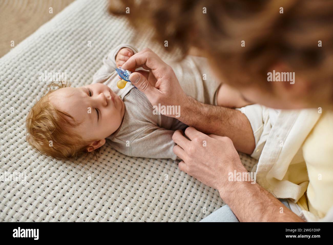 Blick von oben auf den lockigen alleinerziehenden Vater, der seinem kleinen Sohn auf dem Bett einen Schnuller gibt, Vaterschaft Stockfoto