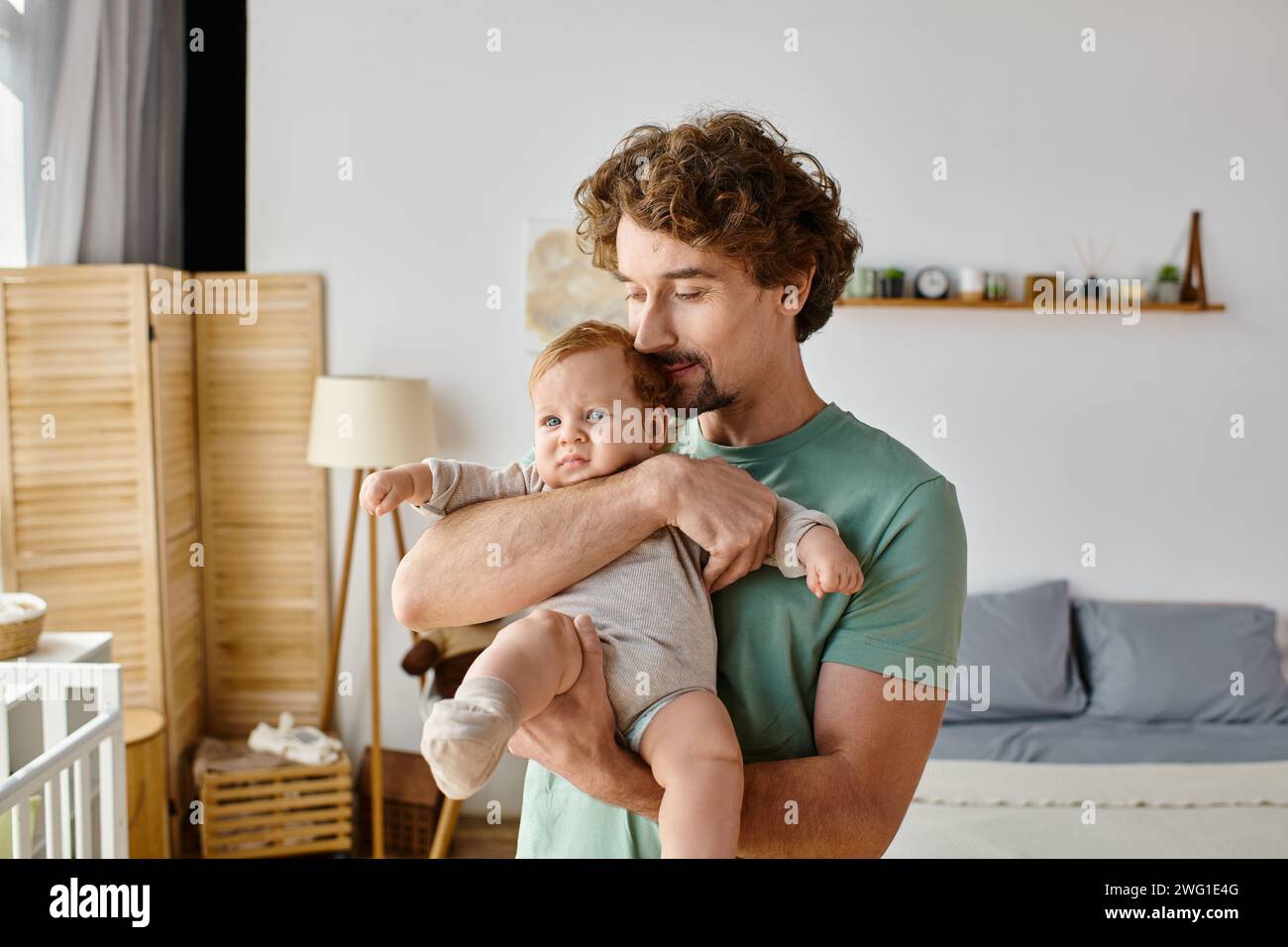 Lockige und fröhliche Vater hält seinen kleinen Jungen in einem gemütlichen Schlafzimmer zu Hause, Vaterschaft Stockfoto