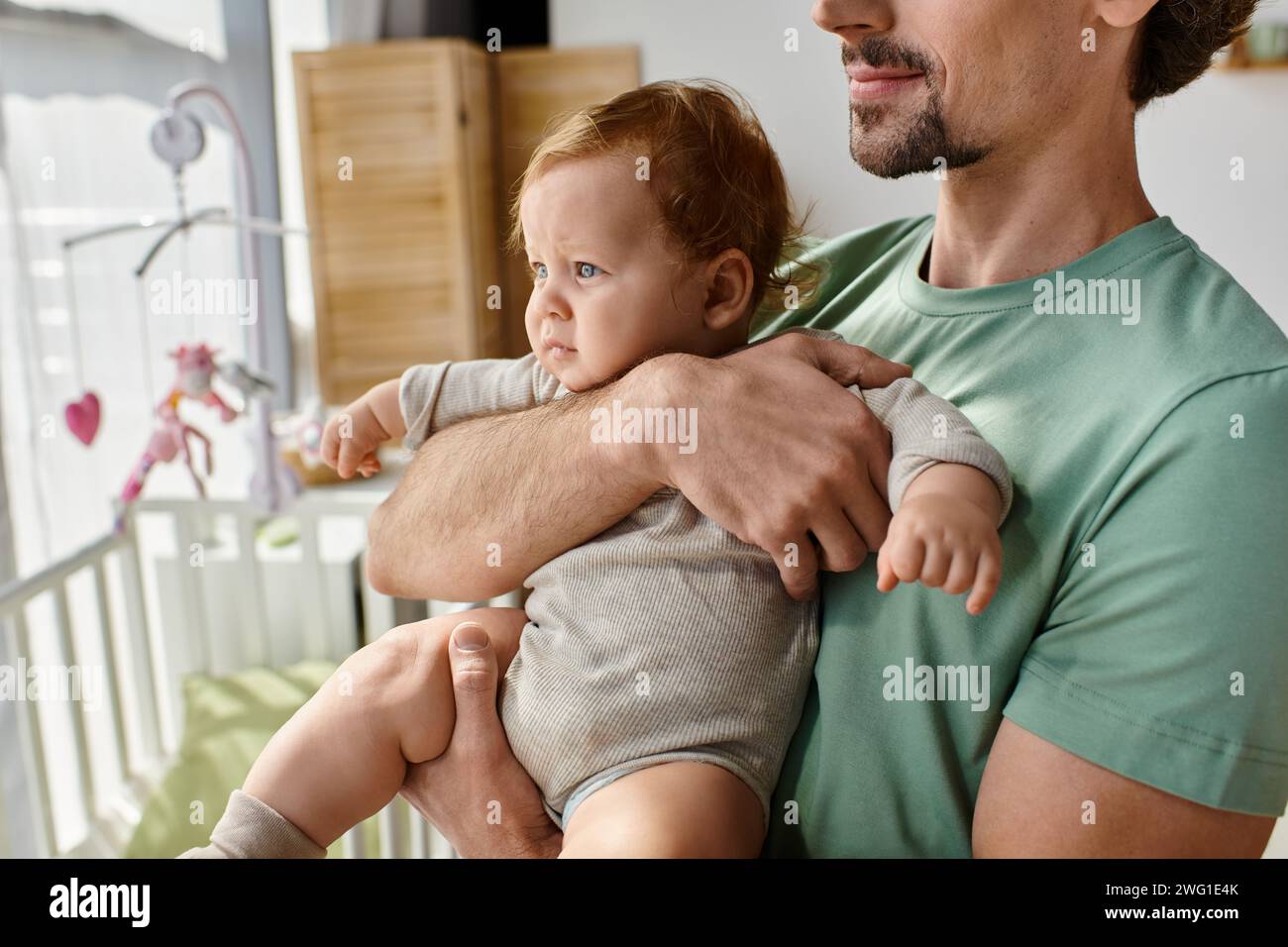 Abgeschnittener Schuss eines bärtigen Vaters, der seinen kleinen Sohn in den Armen hält, in einem gemütlichen Schlafzimmer zu Hause, Vaterschaft Stockfoto
