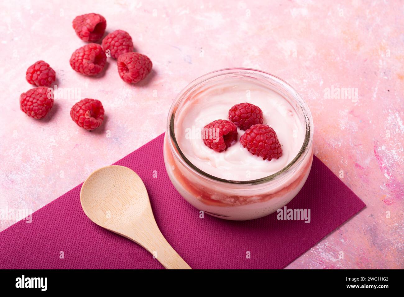 Gesundes Frühstück. Glas mit Bio-Joghurt und frischen Himbeeren auf einem strukturierten Hintergrund Stockfoto