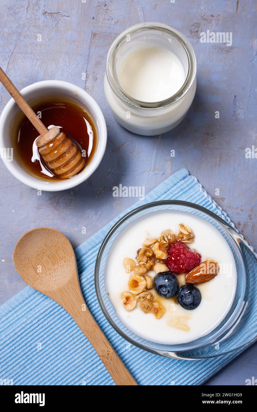 Gesundes Frühstück. Glasschale mit Bio-Joghurt, frischen Himbeeren und Heidelbeeren, Nüssen und Honig auf strukturiertem Holzhintergrund Stockfoto
