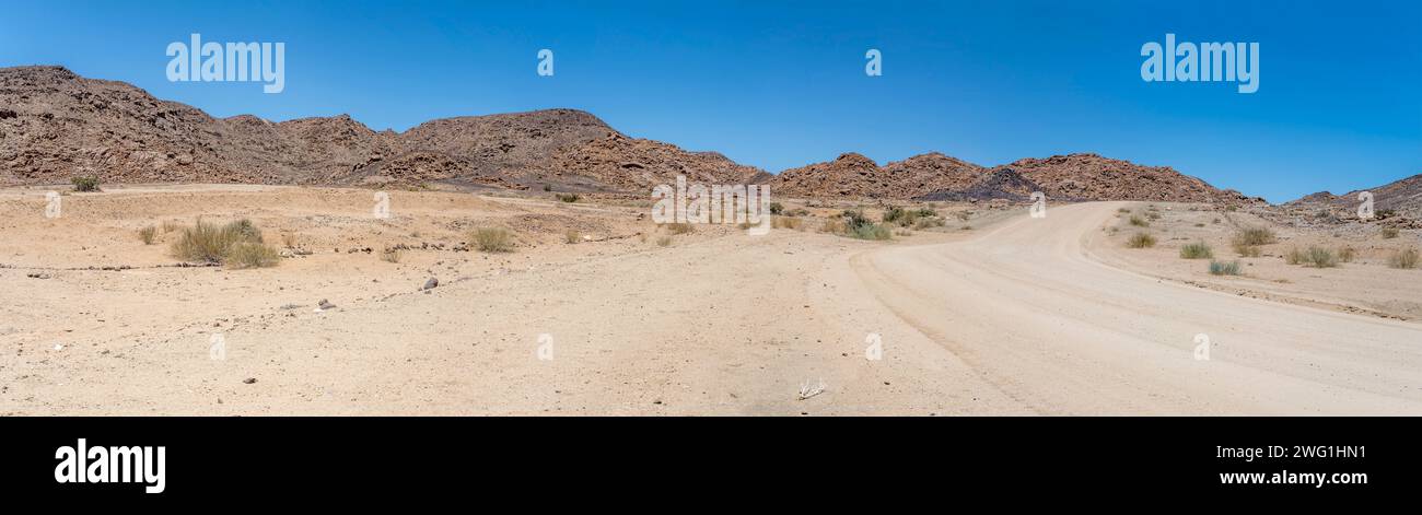 Landschaft mit Schotterstraße und Doleritfelsen in der Wüste, aufgenommen im hellen Licht des späten Frühlings in der Nähe von Hobas, Namibia, Afrika Stockfoto