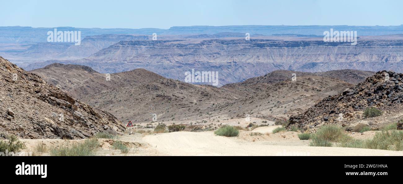 Landschaft mit bergab Schotterstraße in der Wüste mit Fish River Canyon im fernen Hintergrund, aufgenommen im hellen Licht des späten Frühlings in der Nähe von Hobas, Namibia, Afri Stockfoto