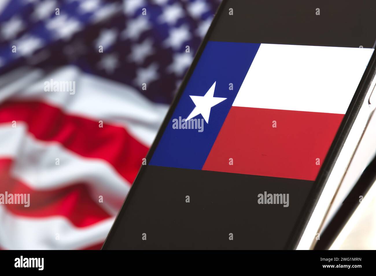 Auf dem Smartphone-Bildschirm wird eine Texas-Flagge mit der amerikanischen Flagge im Hintergrund angezeigt. Stockfoto