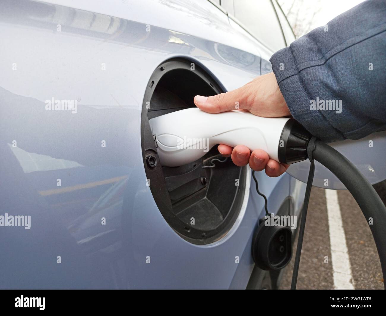 Eine Person, die den Stecker zum Laden eines Elektrofahrzeugs verbindet, um Nachhaltigkeits-, Effizienz- und Innovationskonzepte zu zeigen. Stockfoto