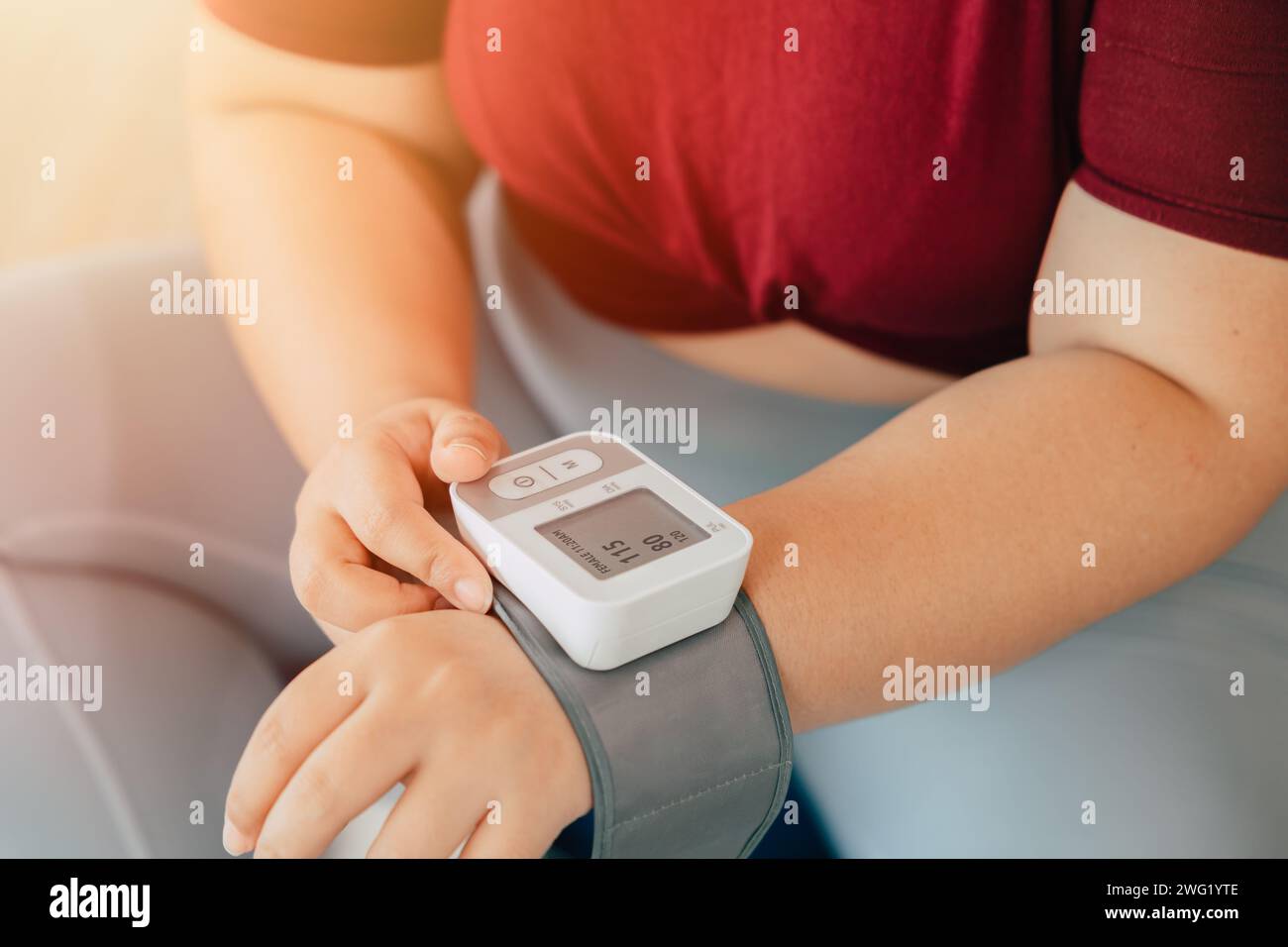 Fette Frauen, die den Blutdruck mit Handgelenkblutgefäßen messen, überwachen moderne häusliche medizinische Geräte Stockfoto