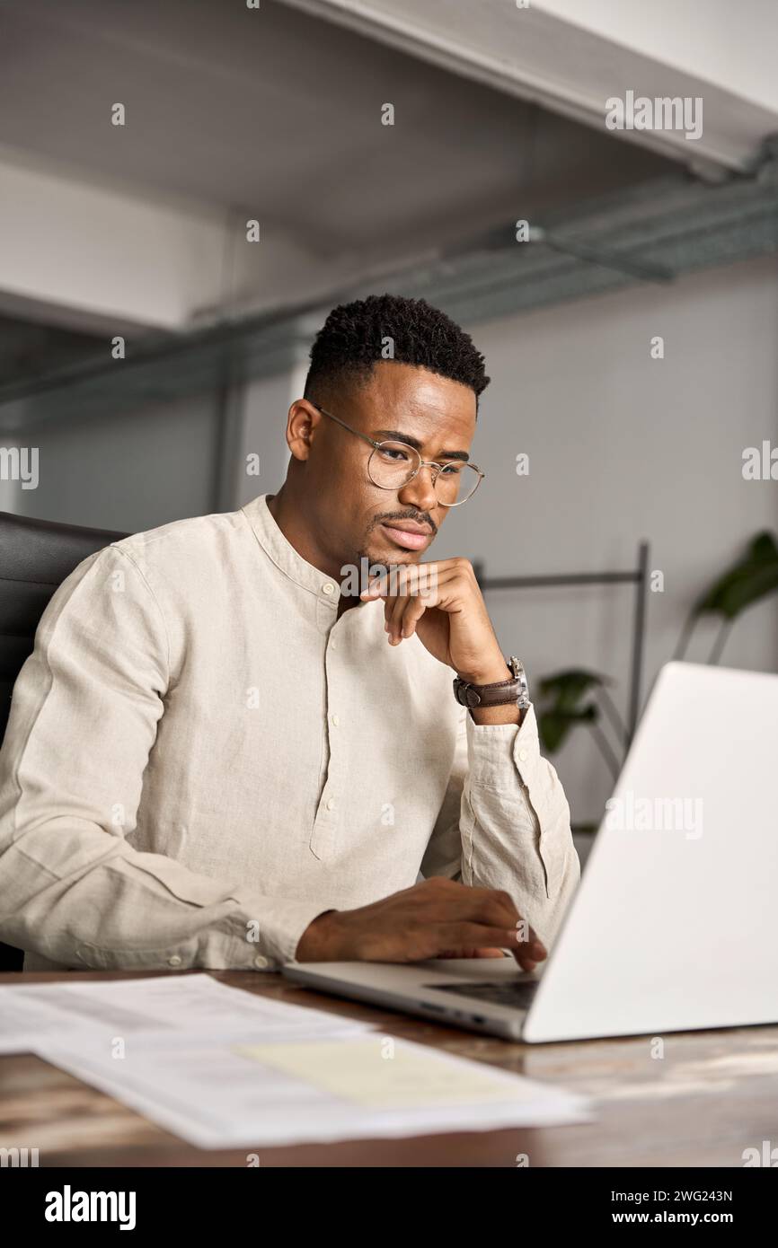 Geschäftiger afrikanischer Geschäftsmann Investor denkt an Laptop, vertikal. Stockfoto
