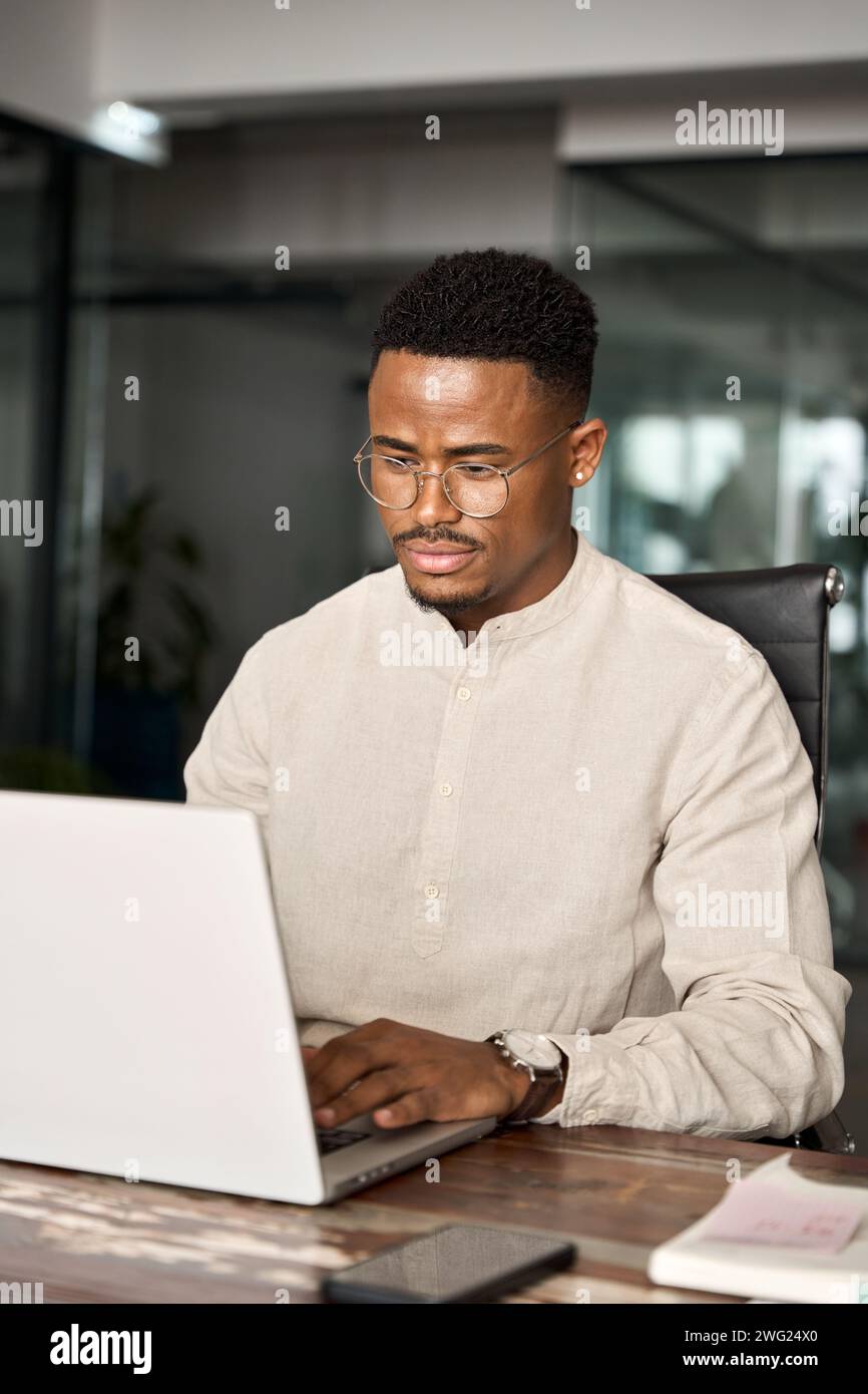 Beschäftigter professioneller afrikanischer Geschäftsmann, der im Büro mit einem Laptop arbeitet. Stockfoto