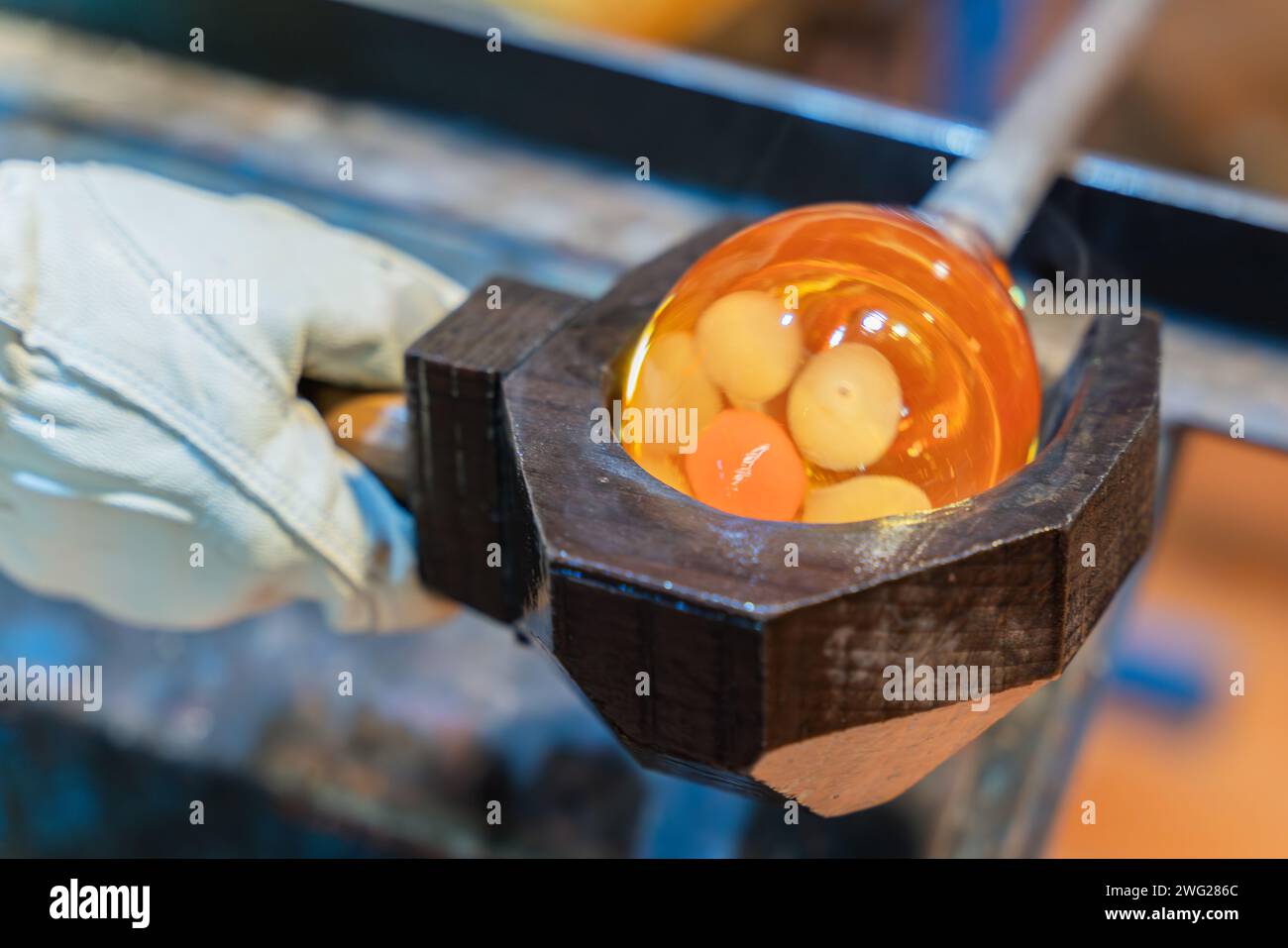 Der Prozess der Glasherstellung. Ein Glasbläser bildet eine Blase aus geschmolzenem Glas. Glasbläser verwenden nasse Holzform zum Formen des rot geschmolzenen Glases Stockfoto