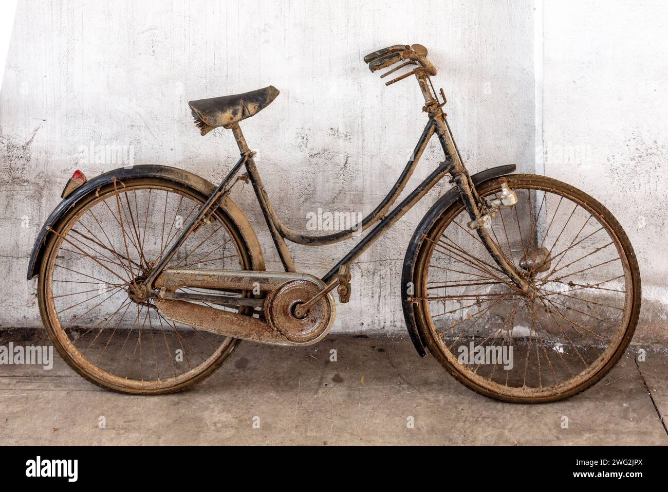 Staubiges, rostiges Fahrrad einer alten Frau, das sich gegen eine weiße Wand lehnt Stockfoto