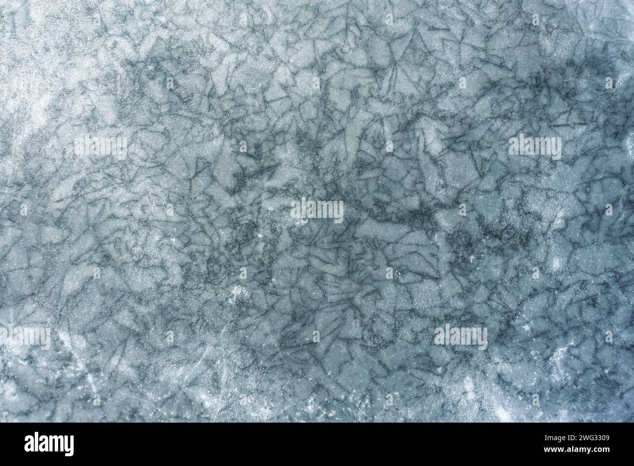 Textur eines gefrorenen Sees mit vielen Rissen auf der Eisoberfläche. Draufsicht. Stockfoto