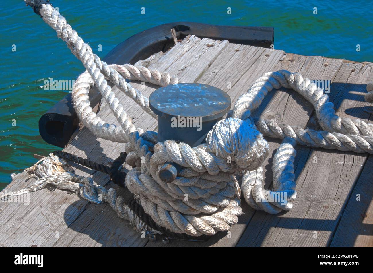 Weißes Sisalseil, das an einem Poller auf einem Holzsteg gewunden ist Stockfoto