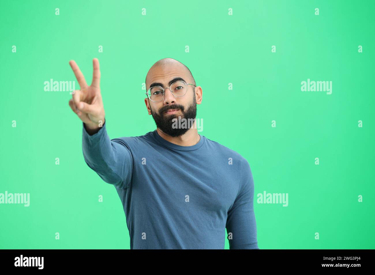 Ein Mann, auf grünem Hintergrund, in Nahaufnahme, zeigt ein Siegeszeichen Stockfoto