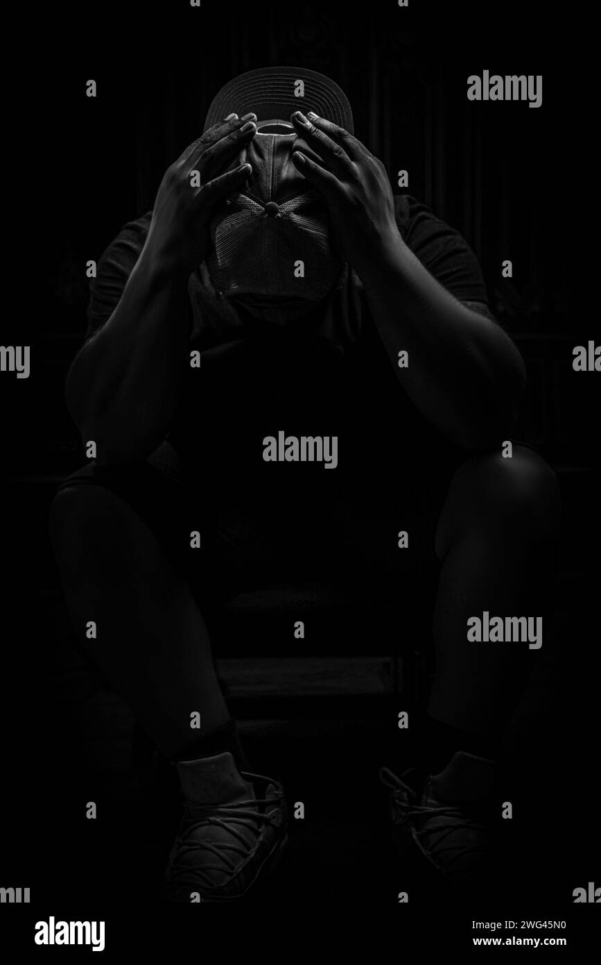 Ein beunruhigter Mann mit Hut, auf einem Stuhl sitzend, mit dem Kopf in den Händen. Stockfoto