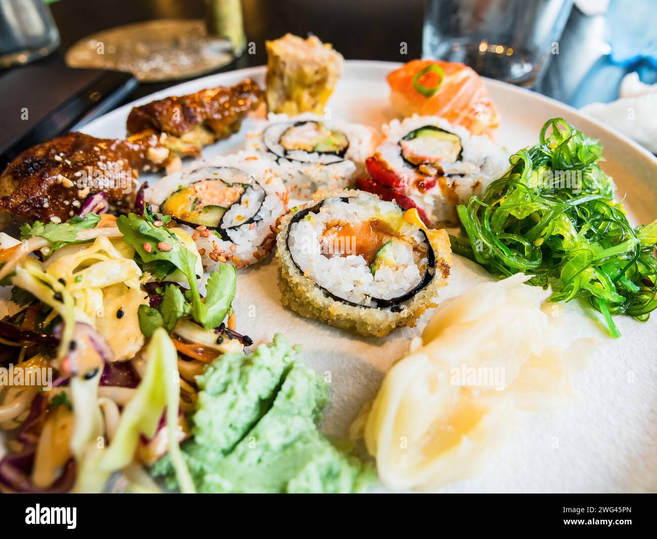 Sushi-Platte mit verschiedenen Stücken einschließlich Maki, Lachnigiri und Wakame. Geringe Schärfentiefe, wobei der zentrale Teil der Platte fokussiert ist. Stockfoto