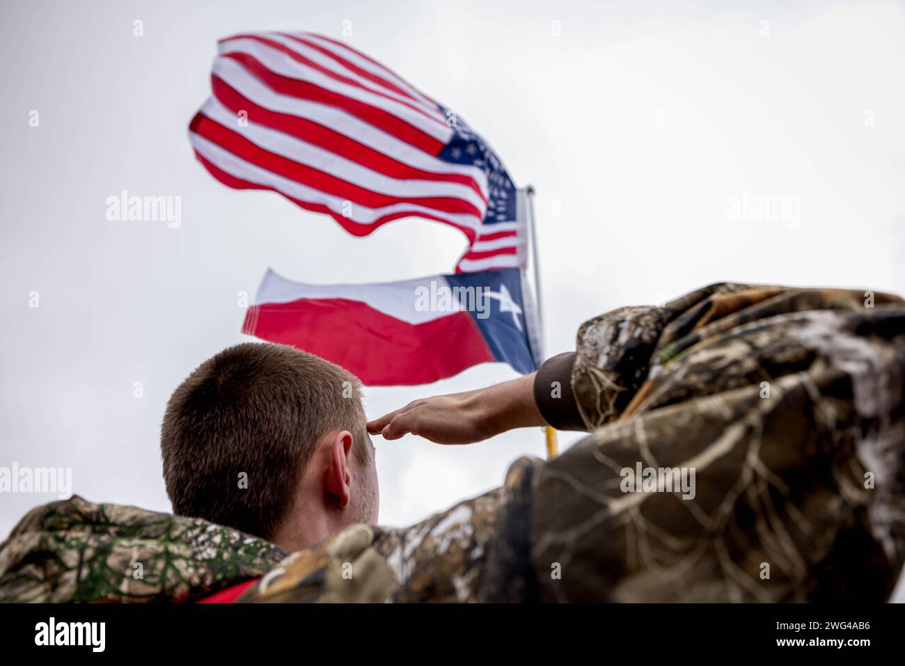 DRIPPING SPRINGS, TEXAS - 1. FEBRUAR: Ein Mann grüßt die amerikanische und texanische Staatsflagge während des „Take Our Border Back“-Konvois am 2. Februar 2024 in Dripping Springs, Texas. wer behauptet, dass "Globalisten" sich verschwören, um die Grenzen der USA offen zu halten, um das Land zu zerstören, macht sich auf den Weg zur Grenze zwischen den USA und Mexiko, während sich der Konflikt zwischen Texas und der Bundesregierung verschärft. (Foto: Michael Nigro/SIPA USA) Stockfoto