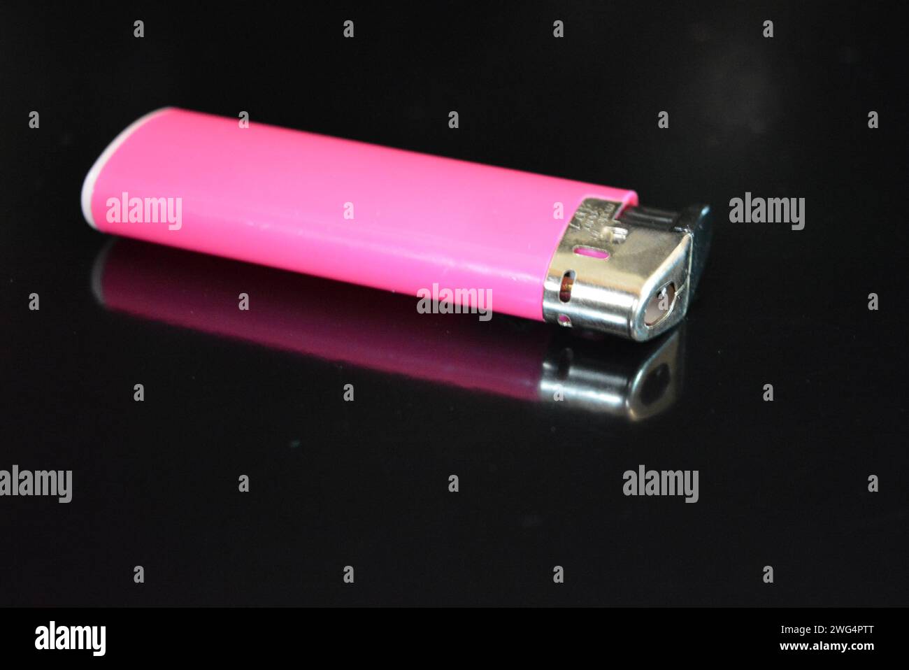 Ein rosafarbenes Kunststofffeuerzeug liegt auf einer glänzend schwarzen Oberfläche. Stockfoto