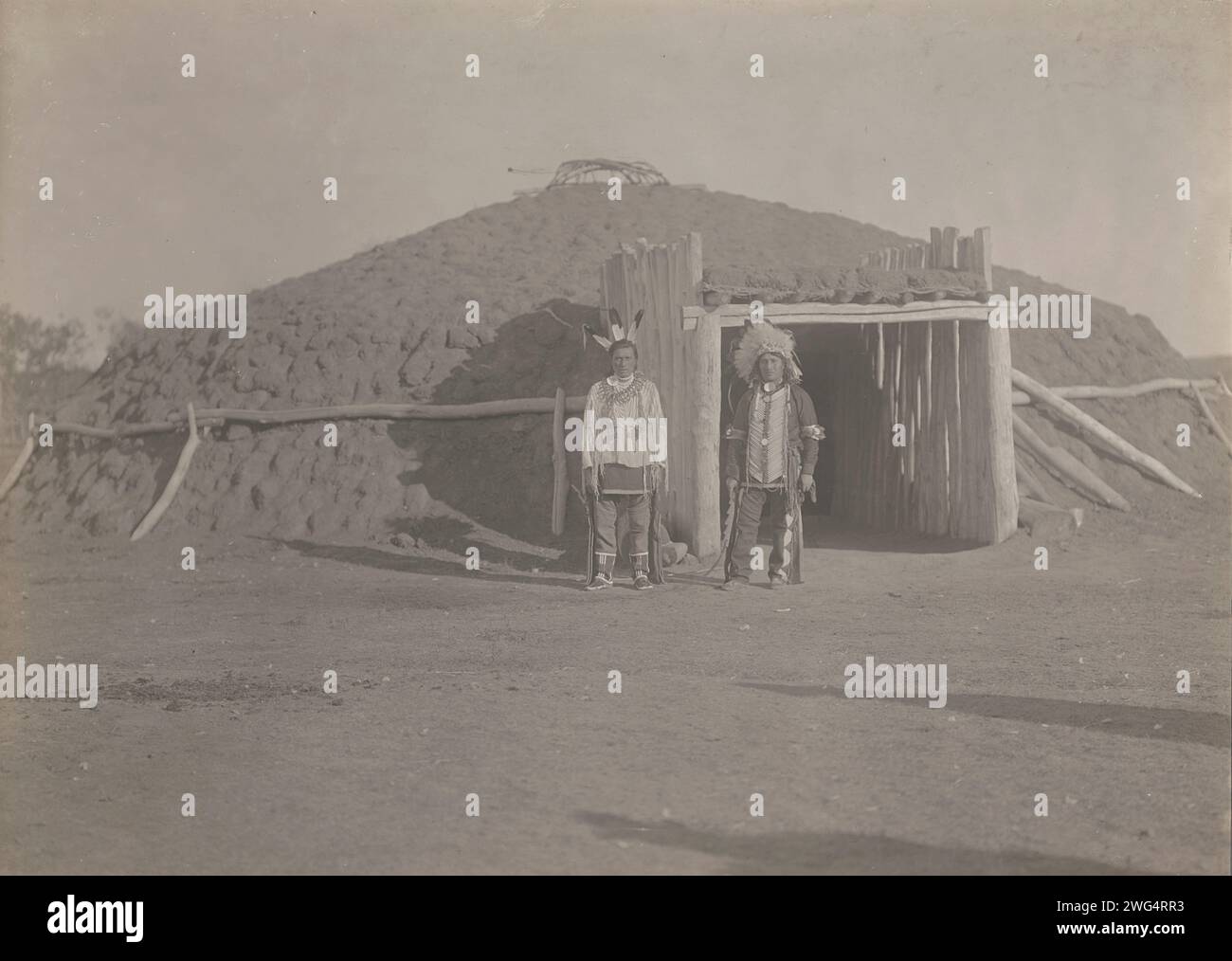 Alfred Chase, 1908. Das Foto zeigt Alfred Chase mit Kopfschmuck und Krähenherz, mit drei Adlerfedern im Haar und einer Halskette mit Bärenkralle, die vor der kuppelförmigen Erdhütte steht. Stockfoto