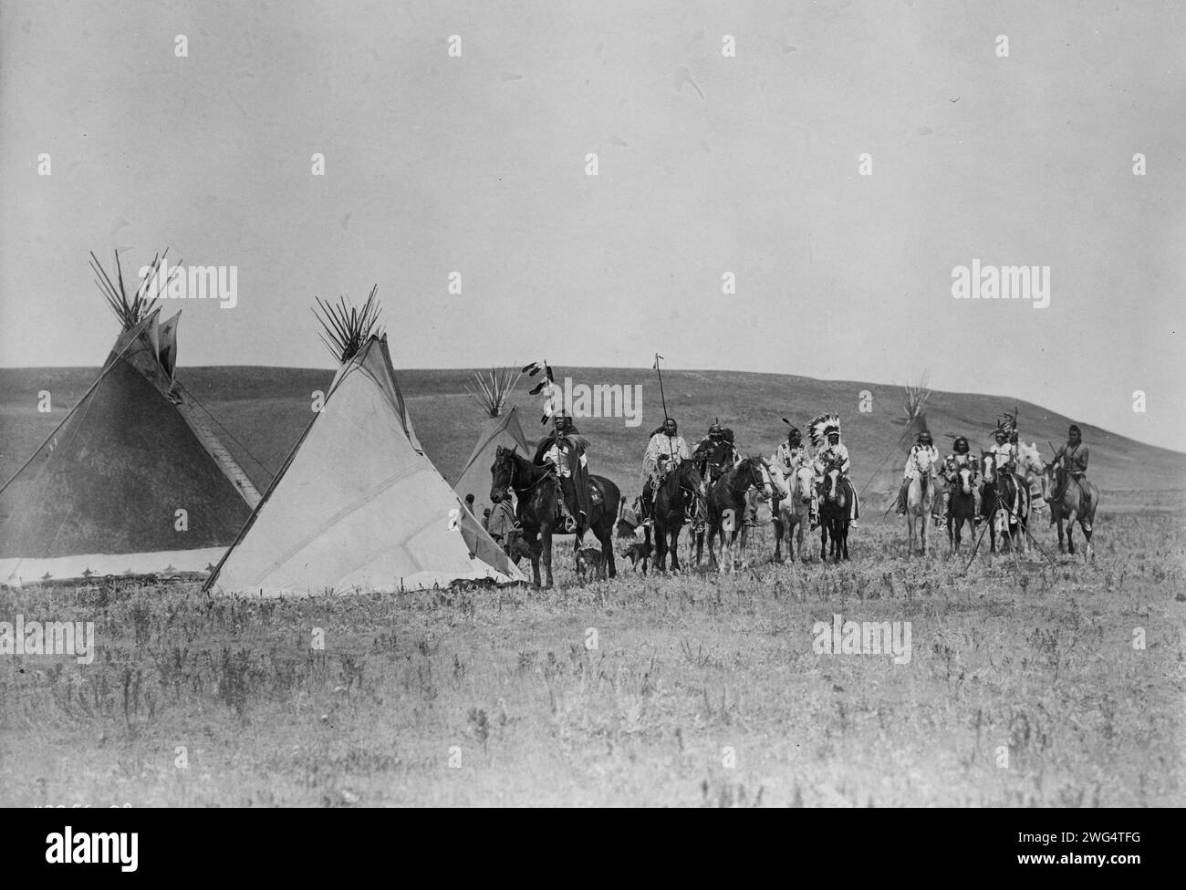 Eine versammelnde Kriegspartei, um 1908. Landschaft mit vier Tipis, elf Atsina-Indianern zu Pferd, drei Frauen, einem Kind und zwei Hunden, Montana. Stockfoto