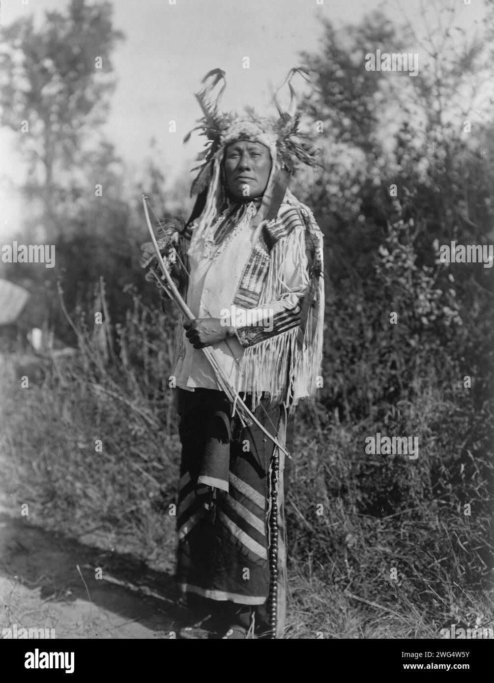 Long Time Dog-Hidatsa, 1908. Langhund, Porträt in voller Länge, stehend, nach vorne gerichtet, Kopfkragen getragen, Hemd aus Buckskin und Leggings mit Messingglocken. Stockfoto