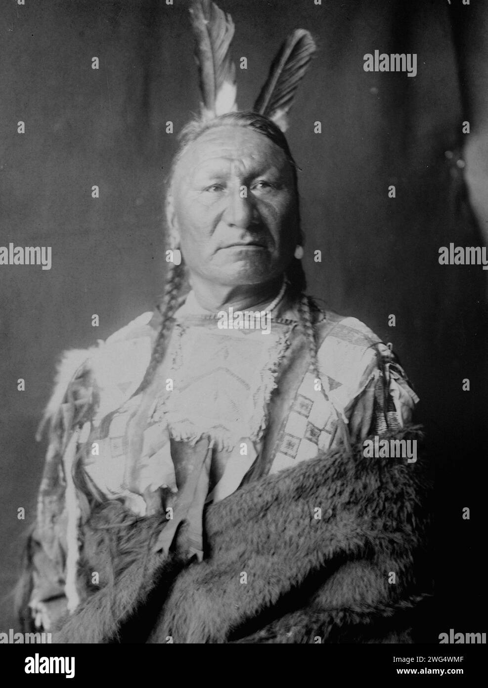 Gelbes Pferd-Yanktonai, halblanges Porträt, stehend, leicht nach rechts gerichtet, mit langen Zöpfen, zwei Adlerfedern im Haar, in Büffelhaut gehüllt, um 1908. Stockfoto