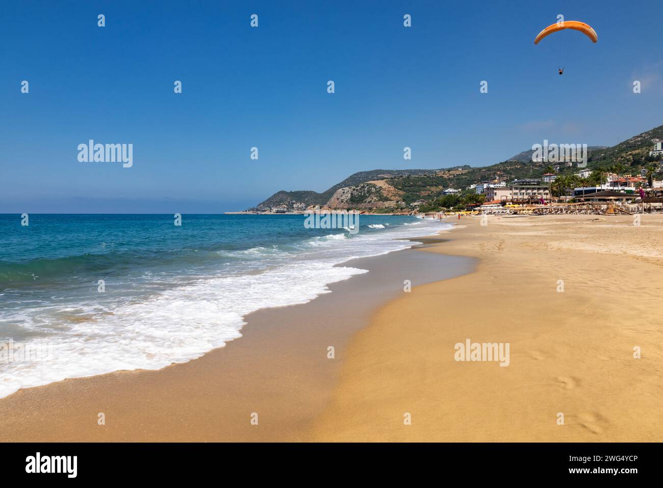 Sonniger Kleopatra Beach in Alanya, Türkei, mit Gleitschirmfliegen und Hotels am Meer im Hintergrund Stockfoto