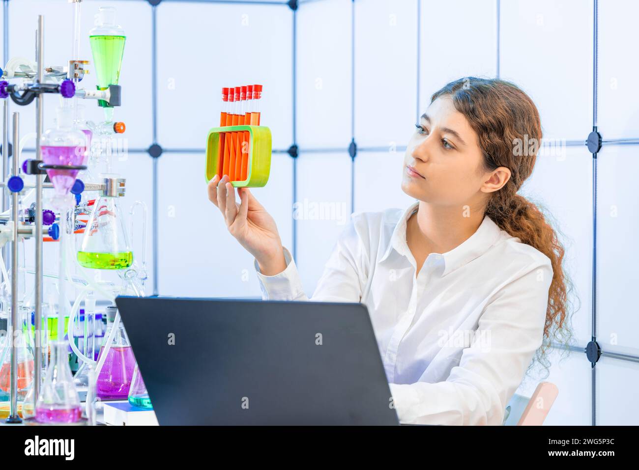 Eine junge Frau in einem Labor für analytische Chemie hält einen Ständer mit Reagenzgläsern in der Hand Stockfoto
