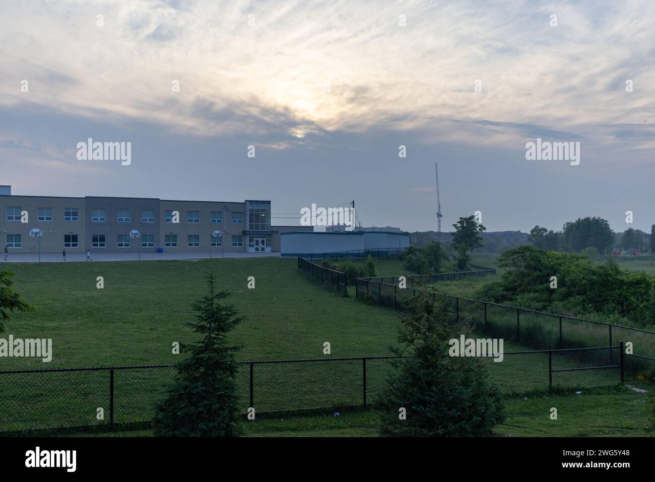 Modernes Schulgebäude - vor dem Hintergrund eines bewölkten Himmels in der Abenddämmerung - umgeben von einem gepflegten grünen Rasen - umgeben von einem schwarzen Zaun. Aufgenommen Stockfoto