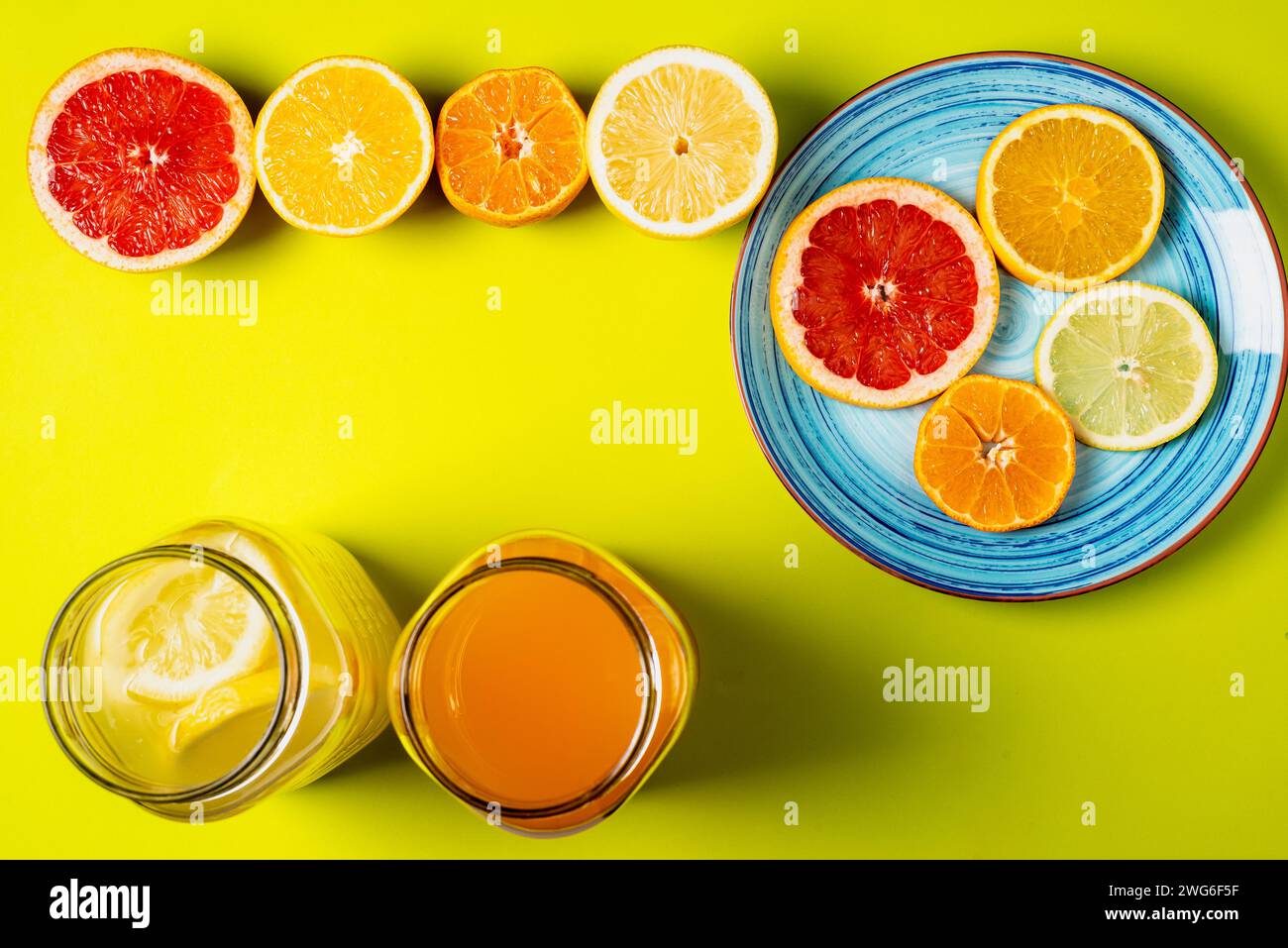 Scheiben von Grapefruit, Orange, Zitrone und Mandarinen auf einem Teller zusammen mit halben Früchten und zwei Gläsern mit Säften, grünlicher Hintergrund. Stockfoto