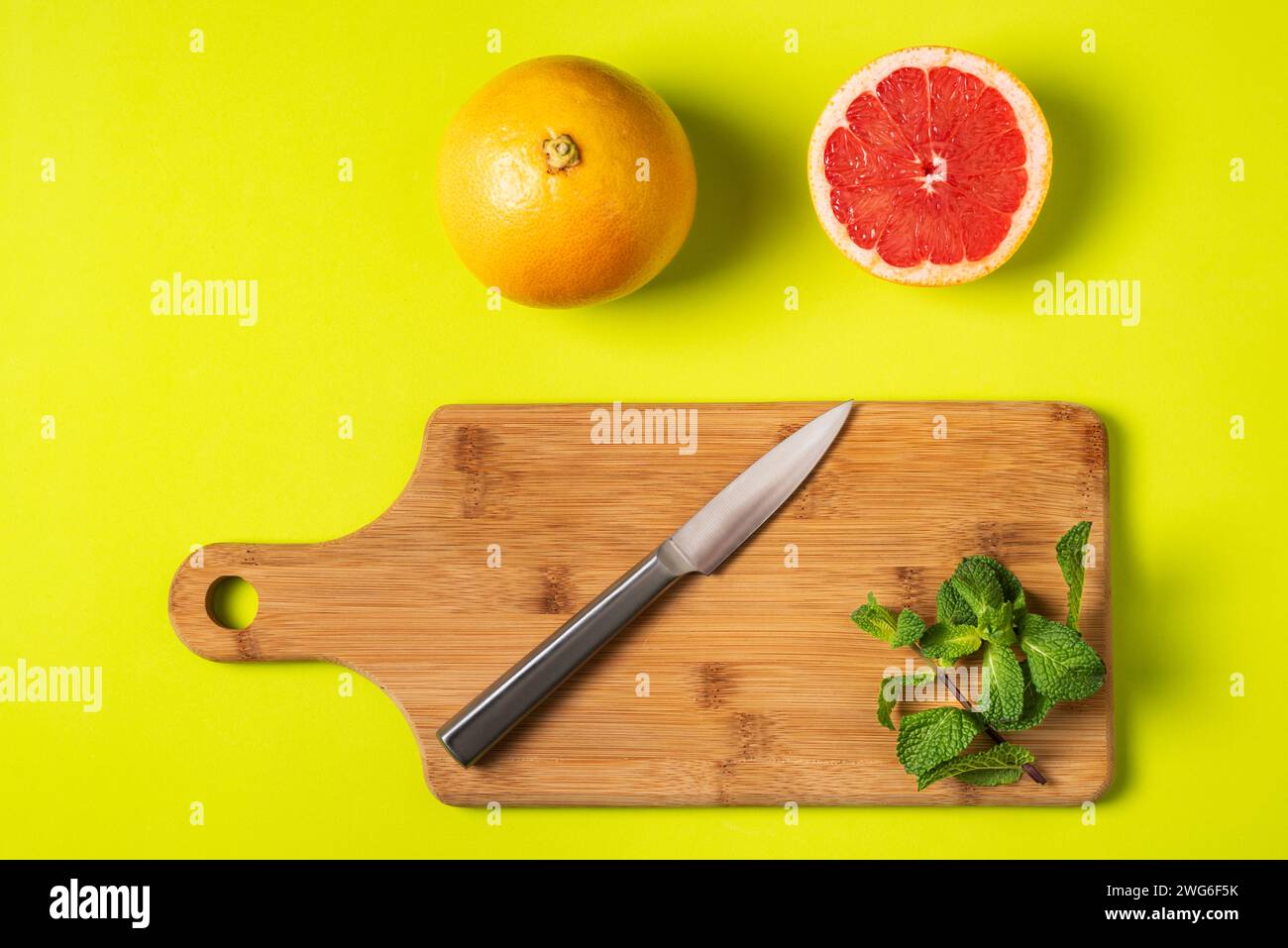 Schneidebrett mit Messer und Pfefferminze, neben einer in zwei Hälften geschnittenen roten Grapefruit und einem weiteren ganzen, grünlichen Hintergrund. Stockfoto