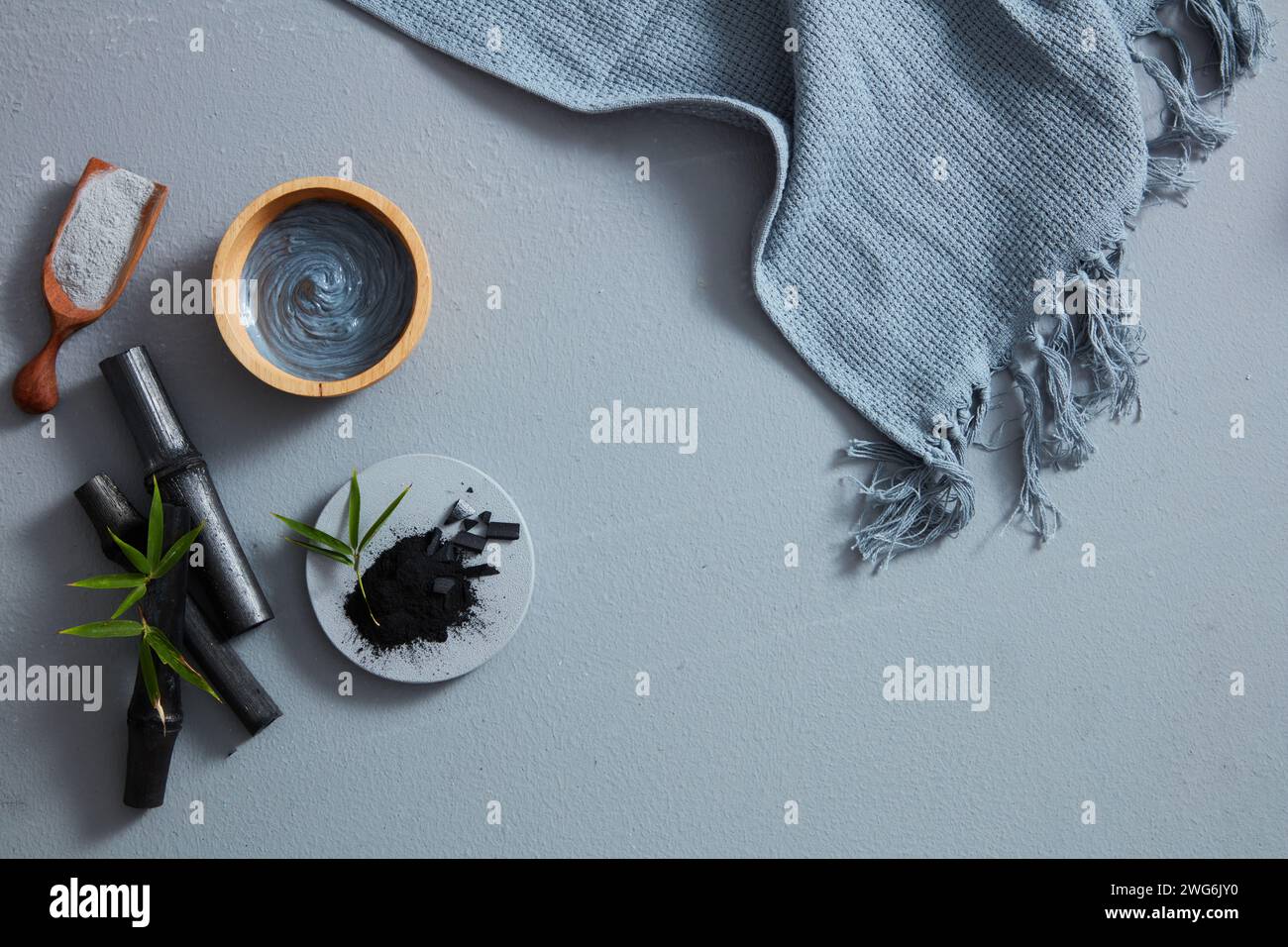 Ein Blick aus der Vogelperspektive auf Holzkohlepulver, Gesichtsmaske und Handtuch auf grauem Hintergrund. Text kann in das leere Feld eingefügt werden Stockfoto
