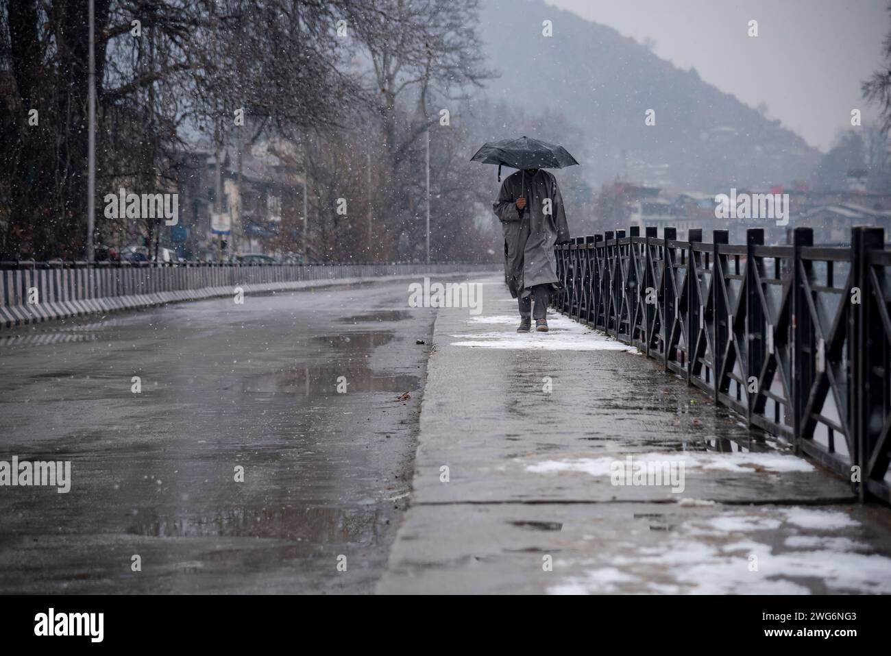 Ein Mann mit einem Schirm, der während des Schneefalls in Srinagar spazieren sah. Die meteorologische Abteilung am Samstag sagt leichte bis mäßige Schneefälle und Regen, insbesondere in höheren Höhen, für die nächsten zwei Tage voraus. Darüber hinaus wurden Lawinenwarnungen für bestimmte Bezirke in der Region ausgegeben. Stockfoto